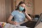 Teenager girl in a medical mask, calls on phone, writes task in notebook, online home training video on Internet, laptop