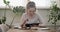 Teenager girl sitting at home at table eating and reading, using digital tablet for learning