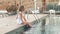 Teenager girl sitting on swimming pool edge dipping legs in water. Happy girl enjoying swimming pool water in summer