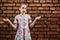 Teenager girl spreads her arms to the side, emotion of surprise on a background of a brick wall