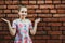 Teenager girl spreads her arms to the side, emotion of surprise on a background of a brick wall