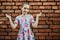 Teenager girl spreads her arms to the side, emotion of surprise on a background of a brick wall