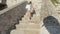 Teenager girl walking up on stairs in stony fortress. Tourist girl in white clothes and sandals climbing on stony