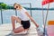 Teenager girl in a white T-shirt and sunglasses on a small wooden pier on the lake shore. Sitting doing stretching