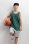 Teenager in green jersey holding basketball and leaning on wall