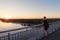 Teenager guy in life style clothes standing near railings on bridge looking at sunset