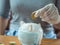 Teenager hand wearing groove putting coin into piggy bank wearing protective mask on the wooden table, saving money for health and