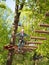 Teenager in helmet and with a safety rope boy goes on suspension bridge made of logs on the blurred background