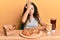 Teenager hispanic girl eating pizza and fried chicken surprised with hand on head for mistake, remember error