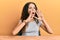 Teenager hispanic girl wearing casual clothes sitting on the table shouting angry out loud with hands over mouth