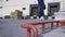 Teenager is jumping and making grind trick on skateboard along red railing in skaterpark. Skateboarder doing nosegrind