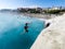 Teenager jumping off on the sea by the rocks with some people looking at him - very dangerous activity and guy doing backflip and