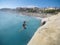 Teenager jumpiong off on the sea by the rocks with some people looking at him - very dangerous activity and guy doing backflip and