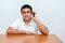 Teenager kid with phone in hand sitting at wood table in home.