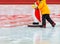 A teenager learns to skate on an ice rink holding on to an assistant, a toy penguin