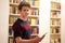 Teenager in library staying in front of bookshelf with smartphone in his hand