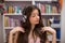 A teenager listens to music with her eyes closed and a bookcase with books in the tel.