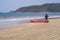 A teenager next to a canoe looking at the ocean on a sandy beach in Goa, India