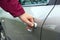 A teenager opens the door of a gray car in the yard during the day..