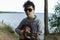 A teenager plays a guitar while sitting on the shore of a lake