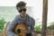 A teenager plays a guitar while sitting on the shore of a lake