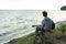 A teenager plays a guitar while sitting on the shore of a lake