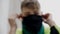 A teenager puts a black protective mask on his face while sitting on a metal ladder.