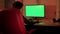 A teenager in a red chair in front of a green computer screen.