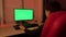 A teenager in a red chair in front of a green computer screen.