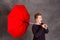 Teenager with red umbrella standing in strong breeze