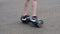 The teenager rides on a self-balancing two-wheeled hoverboard in a circle. Movement on the asphalt. Life style. The legs are close