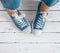 Teenager`s feet in blue color casual new sneakers with white shoelaces on the white wooden floor close up image. Vintage style in