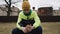 A teenager sits on the background of an industrial zone and holds a phone in his hands.