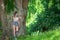 Teenager stands leaning against large tree in natural park