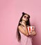 Teenager in striped dress and aviator sunglasses. She is smiling, holding pack of popcorn, posing on pink background. Close up