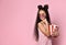 Teenager in striped dress and aviator sunglasses. She is smiling, holding pack of popcorn, posing on pink background. Close up