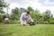 A teenager is trying to do weightlifting with heavy weights in a flowering summer garden.