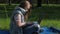 A teenager is typing on a laptop in nature. The girl is sitting on the carpet in the park. A teenage girl on a sunny day with a la