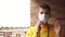 Teenager in a yellow sweatshirt puts on a facial medical mask near a brick wall against a city street