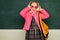 Teenager younf school girl with backpack on blackboard. Portrait of a teen female student. Funny school girl wearing