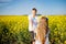 Teenagers: brother and sister with Ukrainian wreath with on head, in rapeseed field under blue sky