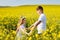 Teenagers: brother and sister with Ukrainian wreath with on head, in rapeseed field under blue sky