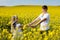 Teenagers: brother and sister with Ukrainian wreath with on head, in rapeseed field under blue sky
