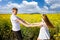 Teenagers: brother and sister with Ukrainian wreath with on head, in rapeseed field under blue sky