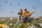 Teenagers with a guitar sittinga on a green hillock with plastic trash on the background of falling plastic debris