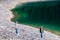 Teenagers stand on stones on the bank of the lake, which reflects the forest, hiking in the forest. Summer vacation.