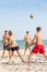 Teenages friends (four people) are playing volleyball on the beach.