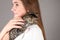 Teengirl holding a baby cat on gray background, cute tenderly smiling, eyes closed. Kitten sits on the female shoulder