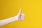 Teens hand with thumb up  on yellow background. Symbol of perfect or accept