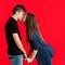 Teens kissing against red backdrop.